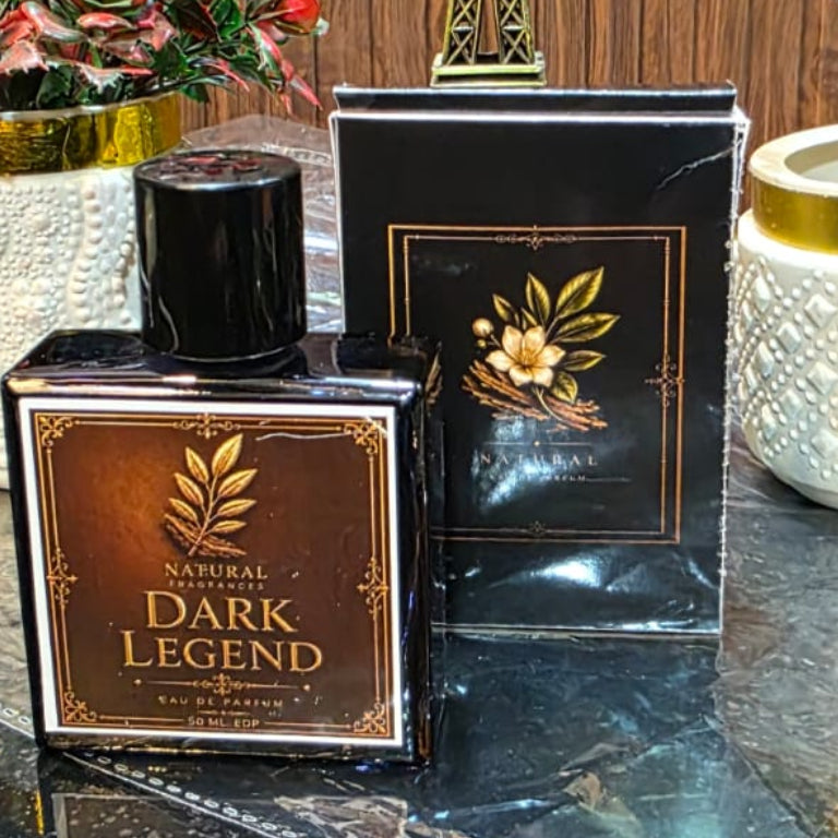 Dark Legend perfume bottle on a reflective surface with decorative plants and a small tower model in the background.