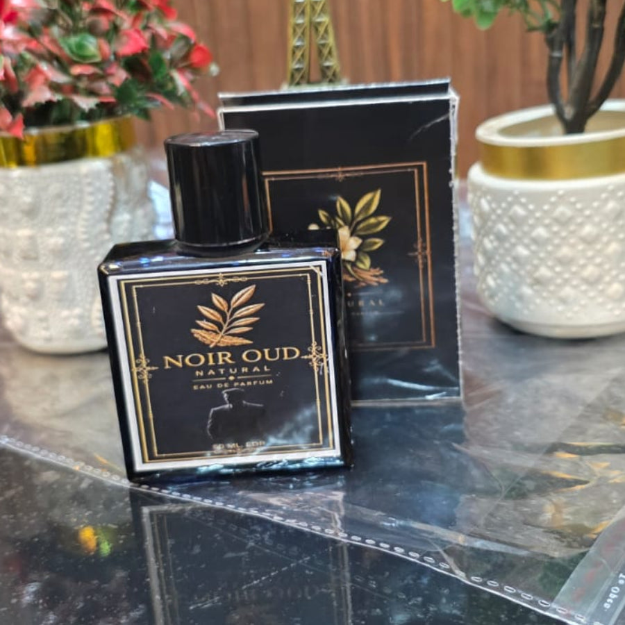 Two black boxes with gold accents on a reflective surface, with decorative plants and a blurred background.