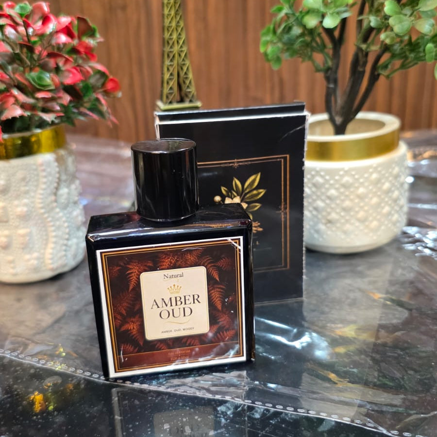 Perfume bottle labeled 'Amber Oud' on a reflective surface with decorative elements in the background.