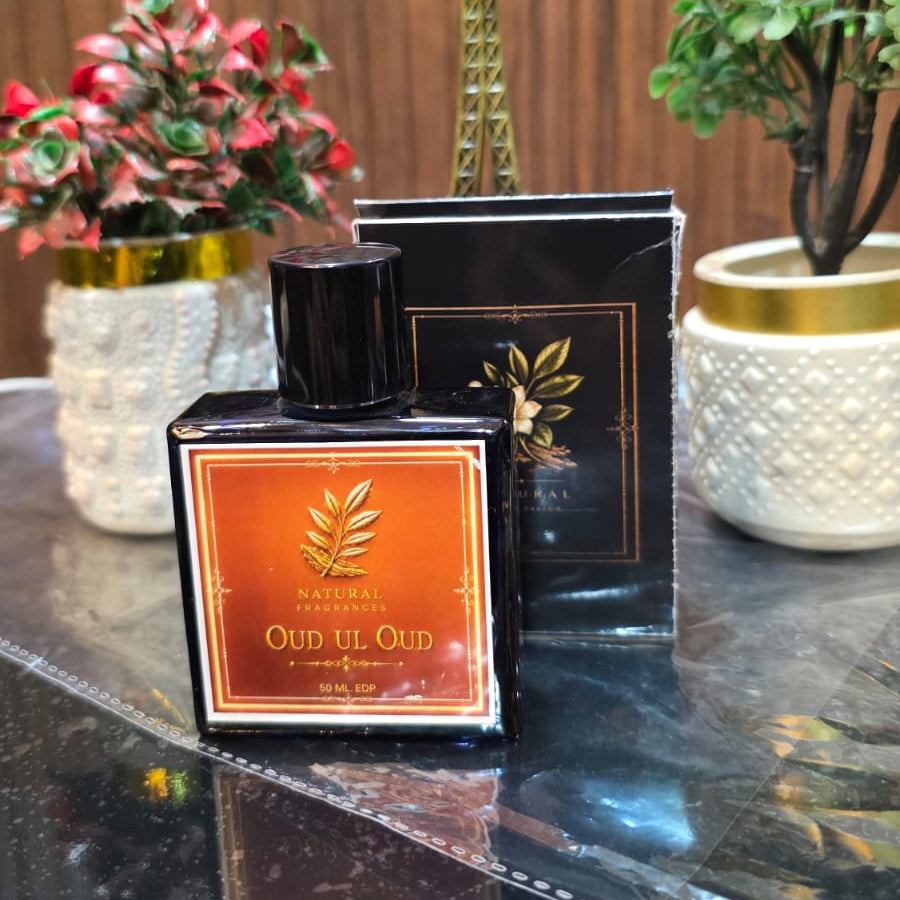 Perfume bottle and packaging on a reflective surface with decorative plants and a small tower model in the background.