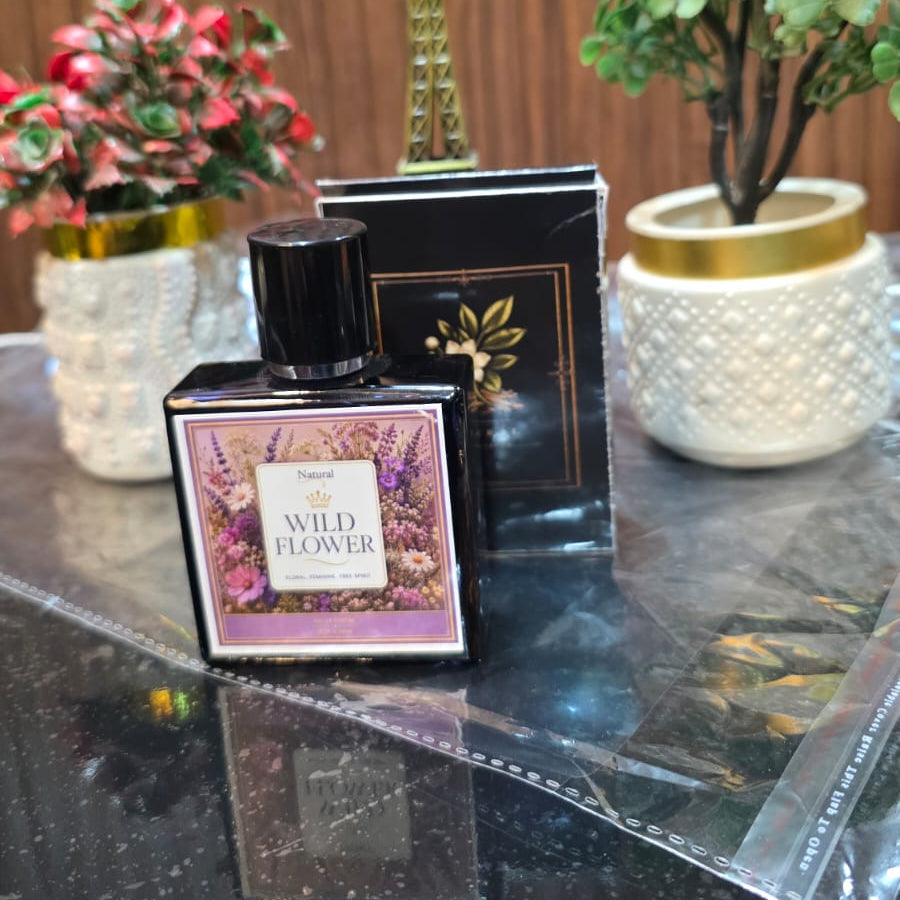 Perfume bottle with decorative packaging on a reflective surface with plants and a small Eiffel Tower model in the background.