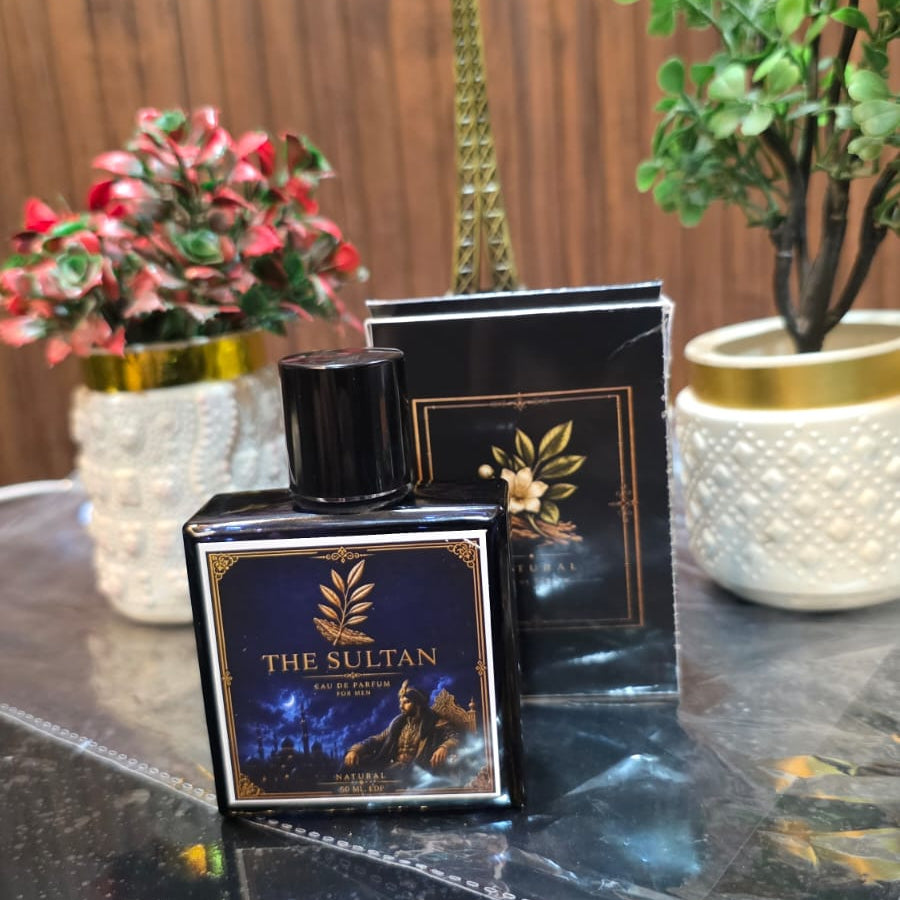 Perfume bottle labeled 'The Sultan' on a reflective surface with decorative plants in the background.