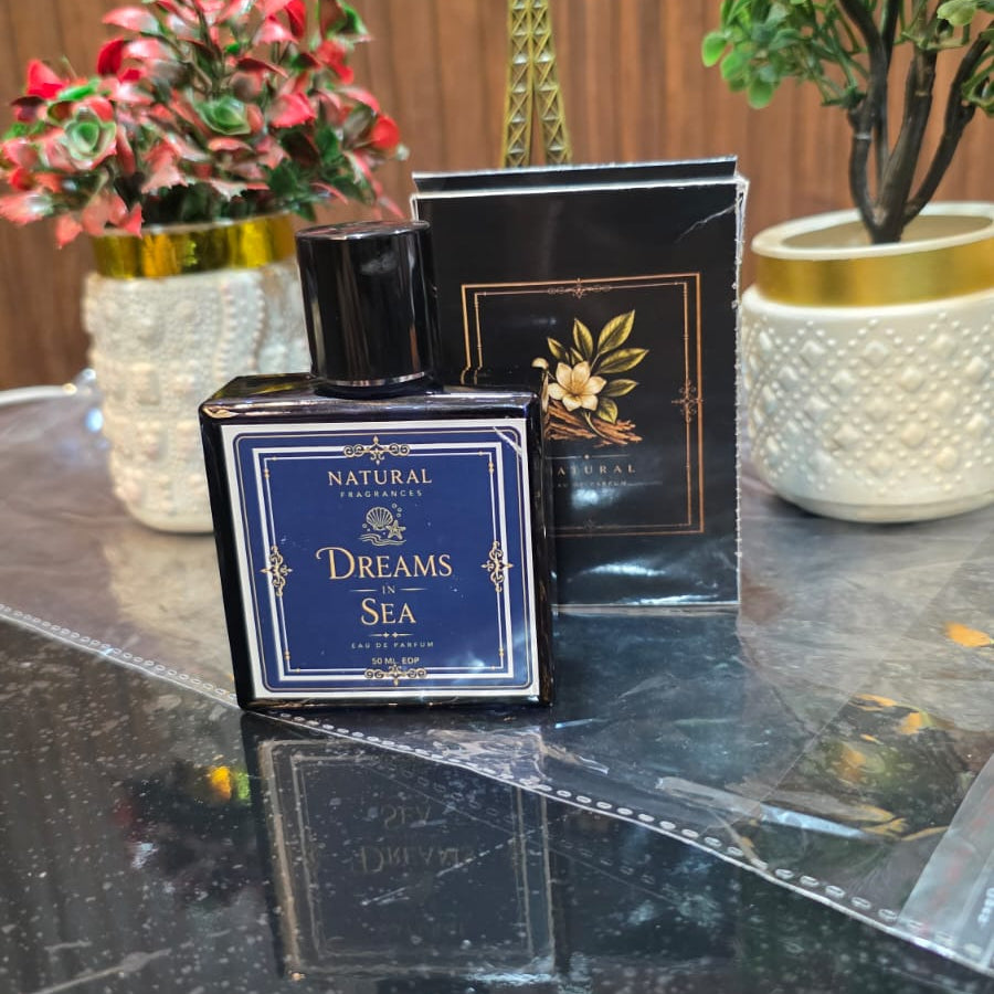 Perfume bottle labeled 'Dreams' on a reflective surface with decorative plants and a small statue in the background.